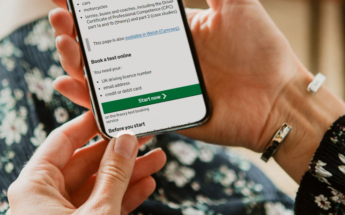 Image of person holding phone with screen showing DVSA web page to book theory test